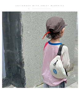 Outdoor shot of child wearing cream canvas chest bag and brown textured baseball cap