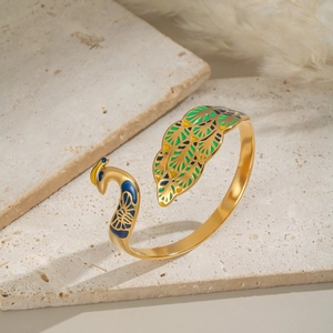 Close-up of golden peacock open bangle with multicolored enamel on textured stone