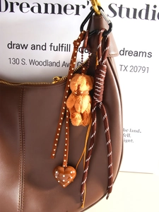 Detail of dark brown leather handbag with plush bear charm and heart rivet strap