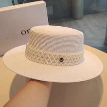 Close-up of white straw boater hat with pearl strap and M-letter metal buckle