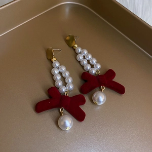 Macro detail of red velvet bow earrings with pearl beads and gold metal accents