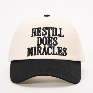 Close-up of HE STILL DOES MIRACLES embroidery on a two-tone cotton baseball cap