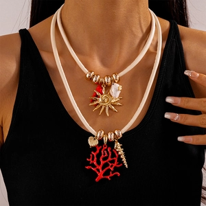 Detail of layered rope necklace with coral, shell pendants and golden sun on black shirt