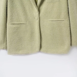 Detail van de zoom en zak van de saliegroene kasjmier blazer met zachte luxe textuur