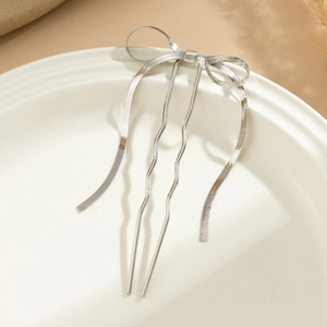 Silver liquid metal bow hair stick accessory displayed on a white ceramic tray