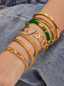 Detail of layered gold bangles featuring green enamel hearts and zircons on denim