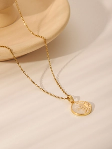 Detail of a gold sun pendant necklace with white mother-of-pearl inlay on ceramic plate