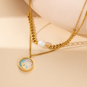Dettaglio di una collana a doppio strato dorata con perla e ciondolo a tema oceanico
