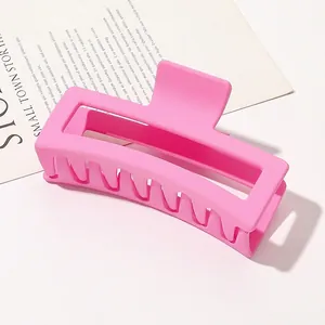 Close-up of a large matte pink rectangular hair claw clip on a minimalist paper background