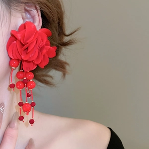 Detail of red fabric flower earrings with beaded tassels worn by a model in close-up