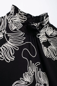 Detail of black embroidered blouse with white leaf patterns and ruffle collar design
