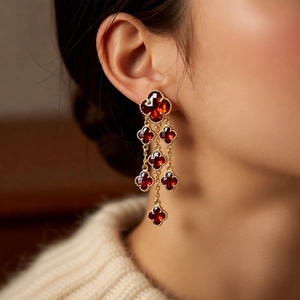 Close-up of gold 18k plated clover earrings with red stones and tassels on model
