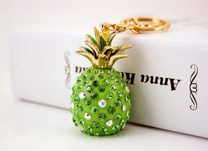 Close-up of green rhinestone pineapple keychain with golden leaves on book prop