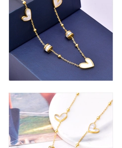 Close-up of gold chain featuring white shell heart charms and zircon cylinder detail