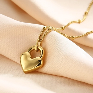 Macro shot of polished gold heart lock pendant on elegant pink silk background