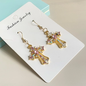 Detailed view of gold cross earrings with pink and purple zircon stones on a white card