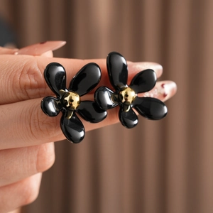 Macro shot of elegant black flower stud earrings with gold center held by hand