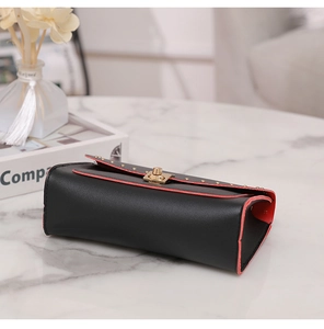 Detail of black pebbled leather bag with orange trim and gold rivet lock on marble