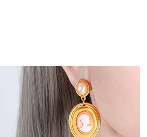 Close-up of golden baroque freshwater pearl earrings with elegant oval cameo pendant detail
