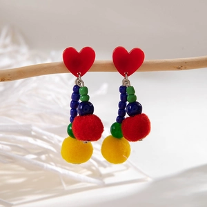 Close-up of colorful beaded Christmas earrings with red heart and soft pom-poms on a branch