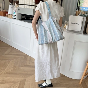 Light blue floral canvas tote bag shown with model in a cozy coffee shop setting