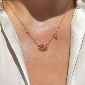 Golden necklace featuring a pink heart gem with star and moon orbital pendants
