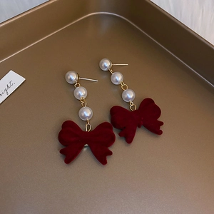 Macro view of velvet red bow earrings with cascading pearls and gold metal accents
