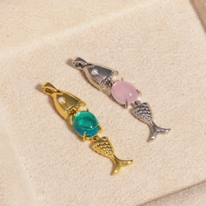 Detail of 18K gold fish charms with green and pink gems and small pearls on a jewelry tray