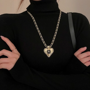 Detail of a heart-shaped gold necklace with black enamel and a number 5 pendant on a model