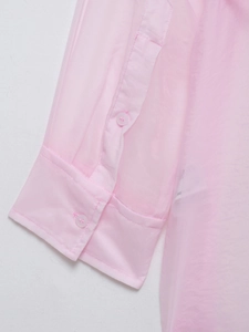 Dettaglio del polsino in organza rosa con bottoni abbinati su camicia velata