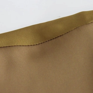 Close-up of golden satin trim and brown fabric stitching on an elegant printed dress