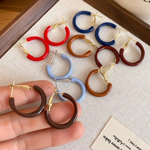 Close-up of colorful resin hoop earrings in red and blue with gold needle clasp