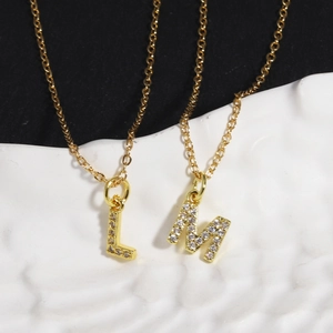 Close-up of gold letter L and M pendants with cubic zirconia on white ceramic tray
