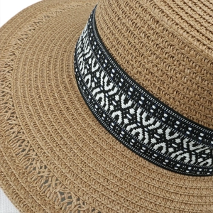 Close-up of natural straw sun hat with ethnic black and white patterned ribbon detail
