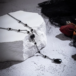 Close-up of gothic black beaded Y-necklace with teardrop pendant on white stone