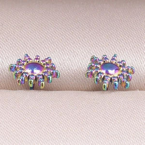 Macro shot of rainbow-plated stainless steel starburst earrings on pink satin padding
