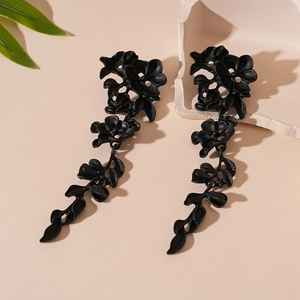Detail view of matte black floral drop earrings on natural stone and leaf background
