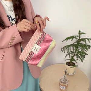 Close-up of pink and yellow striped woven cosmetic bag held by a model in a pink suit