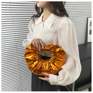 Detail einer hellorangen metallischen Faltenhandtasche mit kreisförmigem Ringgriff