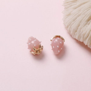 Dettaglio di due ciondoli fragola rosa con ganci foglia oro su sfondo rosa tenue