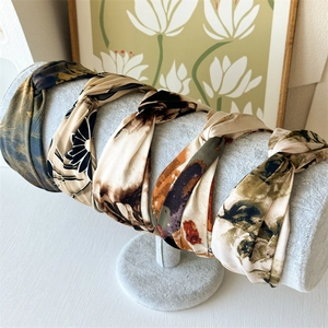 Five vintage earth-tone printed twist headbands displayed on a premium grey velvet stand
