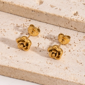 Minimalist gold rose-shaped stainless steel earrings on a textured stone display