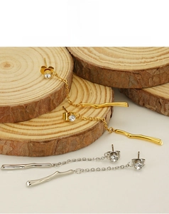 Close-up of gold and silver bamboo tassel earrings with rhinestones on a wood base