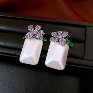 Nahaufnahme von Perlenohrringen mit funkelnden lila Blumenkristallen und grünen Blättern