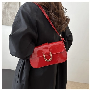 Chic red patent leather shoulder bag with gold hardware worn over a black winter coat