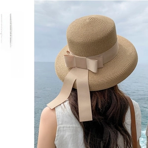 Detail of khaki straw sun hat with beige ribbon against a scenic ocean background
