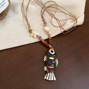 Detail of bohemian ceramic fish pendant with wooden beads and starfish on woven rope