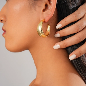 Close-up of a model wearing large chunky gold C-shaped hoop earrings with a mirror finish