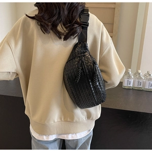 Close-up of black woven leather chest bag with zipper detail and adjustable strap