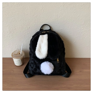 Close-up of cute rabbit-shaped plush backpack in black and white on a wooden table